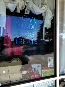 Neon lights reading HOME MADE DOG TREATS welcome customers who take a peek inside the storefront.